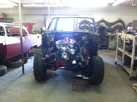 1982 Ford Bronco - 1982 Ford Bronco chassis undergoing work, engine and suspension visible. Another vehicle is in the background.