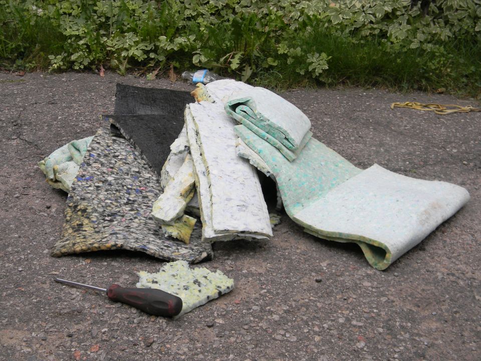 Pile of torn jute and foam seat padding on pavement next to a screwdriver