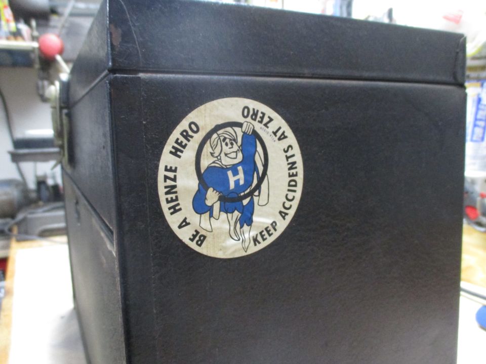Black case with a round sticker showing a cartoon character with an H on its chest, wearing a cape, and text that says 'BE A HENZE HERO KEEP ACCIDENTS AT ZERO'