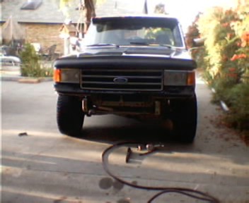 1991 Ford Bronco - Head-on view of a lifted black Ford truck with a white roof sitting in a driveway, showing the stock grille with Ford lettering, amber turn…