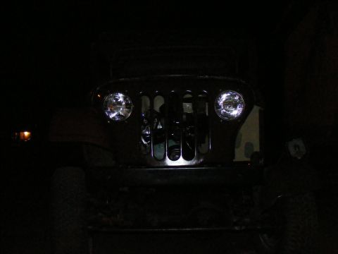 Front view of a Jeep CJ-5 grille with aftermarket headlights at night