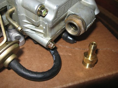 1981 Ford Bronco - Close-up of a carburetor component with a brass fitting and hose attached, resting on a brown surface.