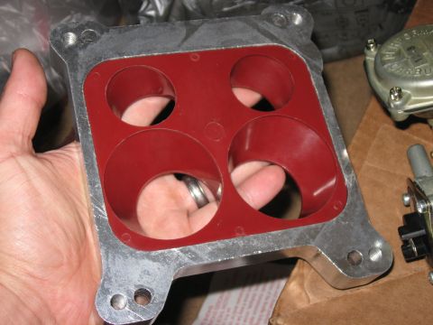1981 Ford Bronco - A hand holds an aluminum carburetor spacer with a red gasket, showing four intake ports.
