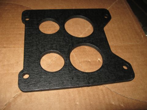 1981 Ford Bronco - A black carburetor gasket with four holes is shown against a cardboard background.