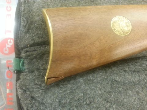 1995 Ford Bronco - Close-up of a rifle stock a wooden finish and a decorative Indian head medallion.