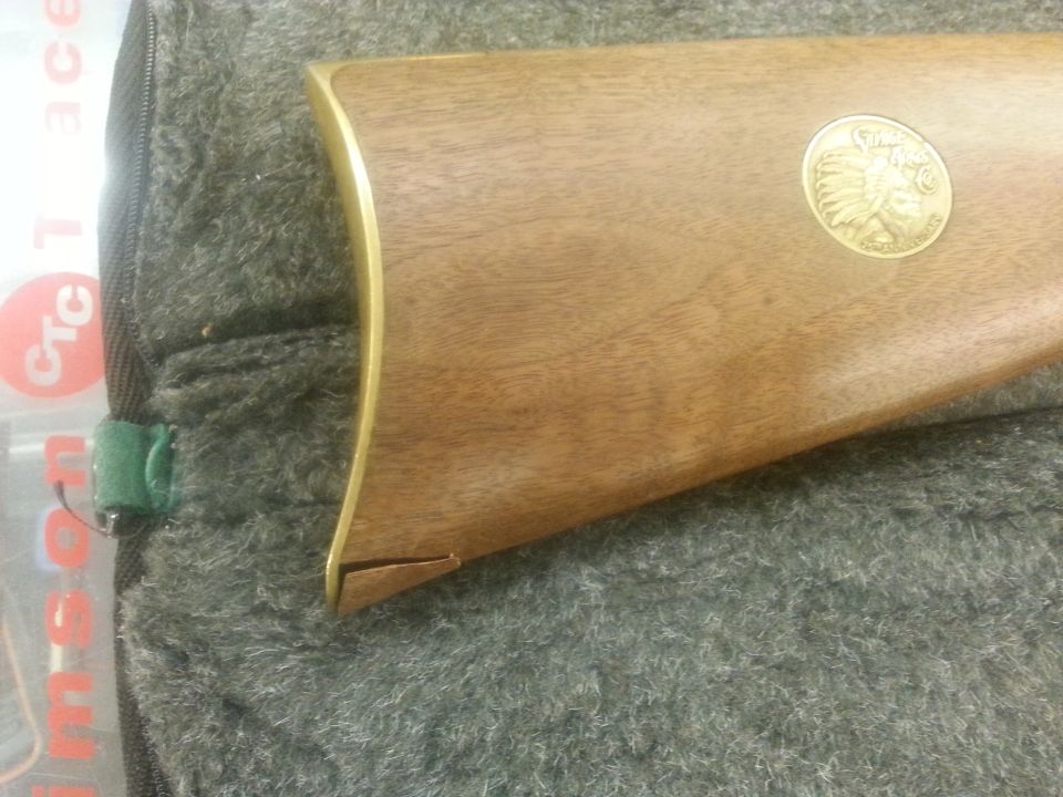 Wooden rifle stock with brass trim and a round medallion showing an Indian head