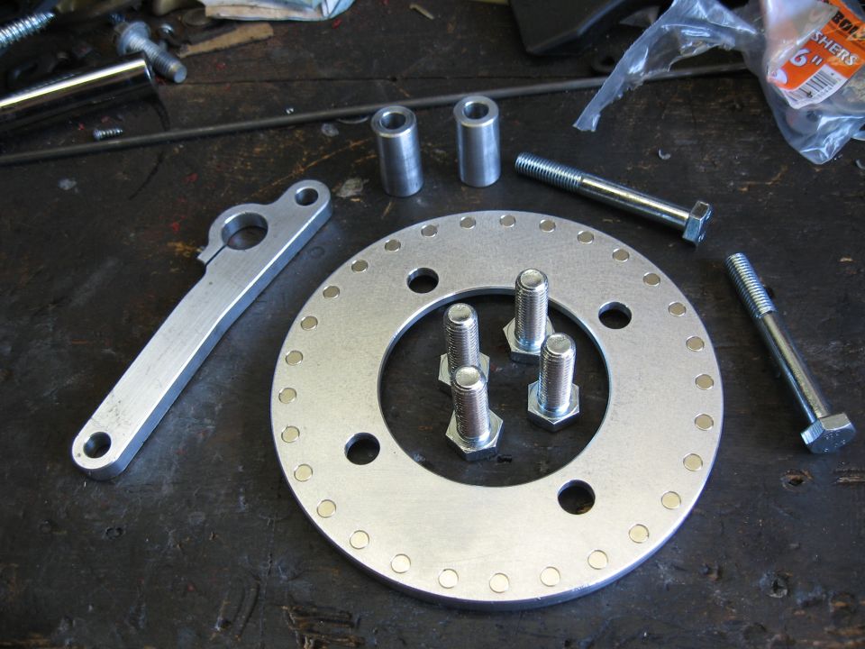 Metal bracket, circular plate with bolts, and two spacers on a workbench