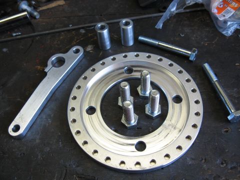 1994 Ford Bronco - Various metal components, including a large ring and bolts, are laid out on a workbench, likely for assembly.