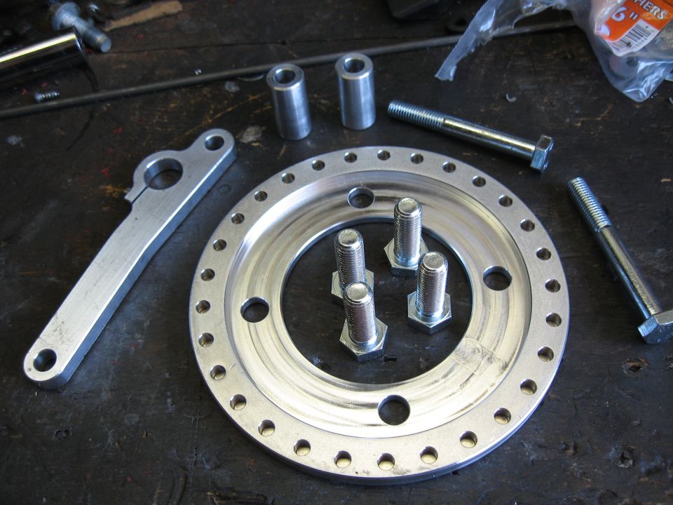 Metal disc with many bolt holes, a bracket, bolts, and spacers on a workbench