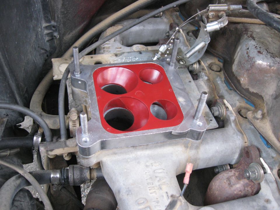 Close-up of a carburetor base plate with a red gasket on an engine intake manifold