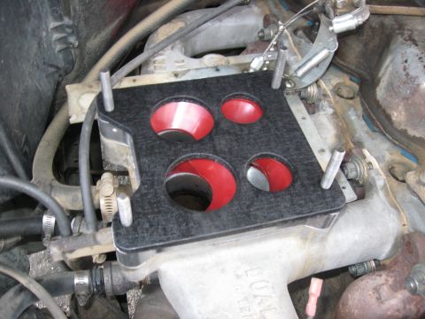 1981 Ford Bronco - Close-up of a black carburetor adapter plate with red inserts, installed on an engine intake manifold.