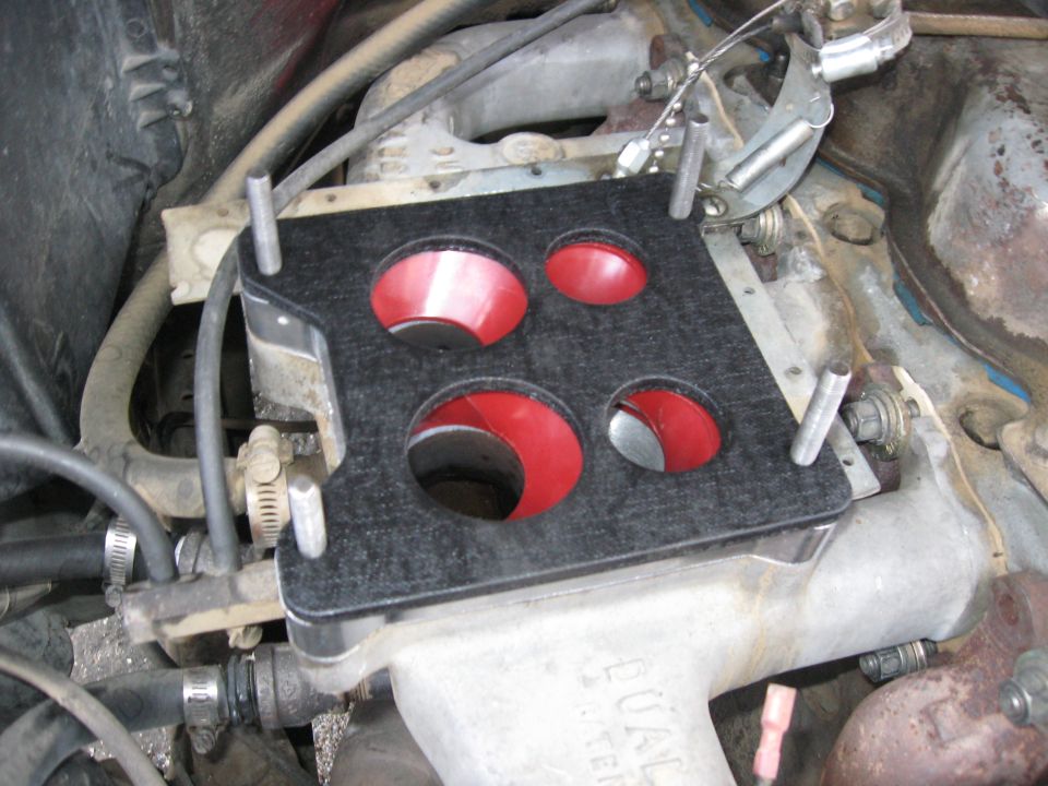 Black carburetor adapter plate with four red-lined openings, mounted on engine intake
