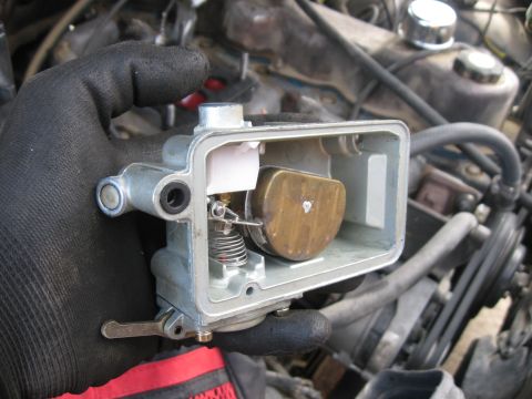 1981 Ford Bronco - Carburetor part being held with engine components in the background.