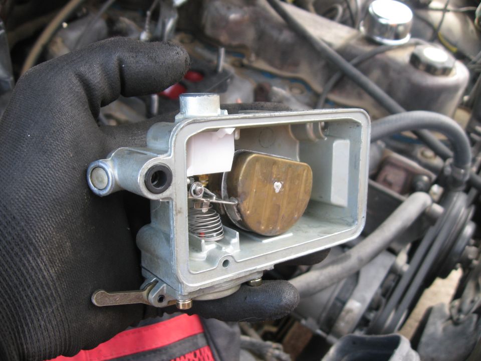 Gloved hand holding a carburetor with brass float visible inside