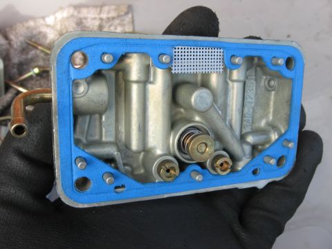 1981 Ford Bronco - A carburetor part is held in a gloved hand, showing internal components and a blue gasket.