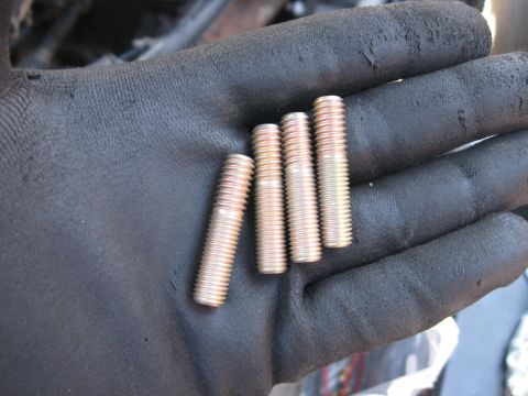 1981 Ford Bronco - Gloved hand holding four threaded metal studs, likely for automotive repair.