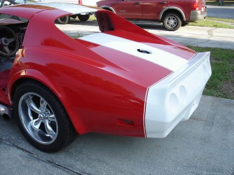 1976 Chevrolet Corvette - Rear view of a red and white 1976 Chevrolet Corvette, racing stripes and a spoiler, with another vehicle visible in the background.