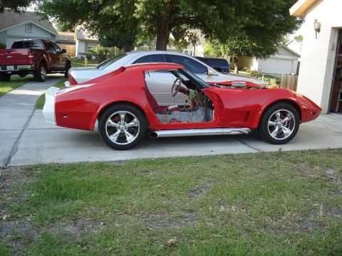 1976 Chevrolet Corvette - A red sports car is undergoing repairs, with its doors and hood open, parked in a driveway.