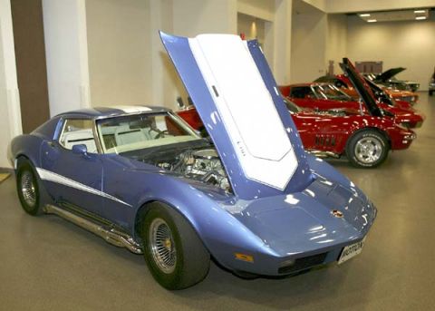 1976 Chevrolet Corvette - A blue 1976 Chevrolet Corvette is displayed with its hood open, parked indoors with other vehicles visible in the background.