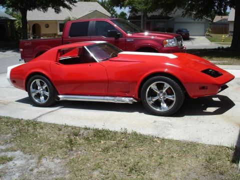1976 Chevrolet Corvette - A red 1975 Chevrolet Corvette is parked in front of a red pickup truck on a driveway.