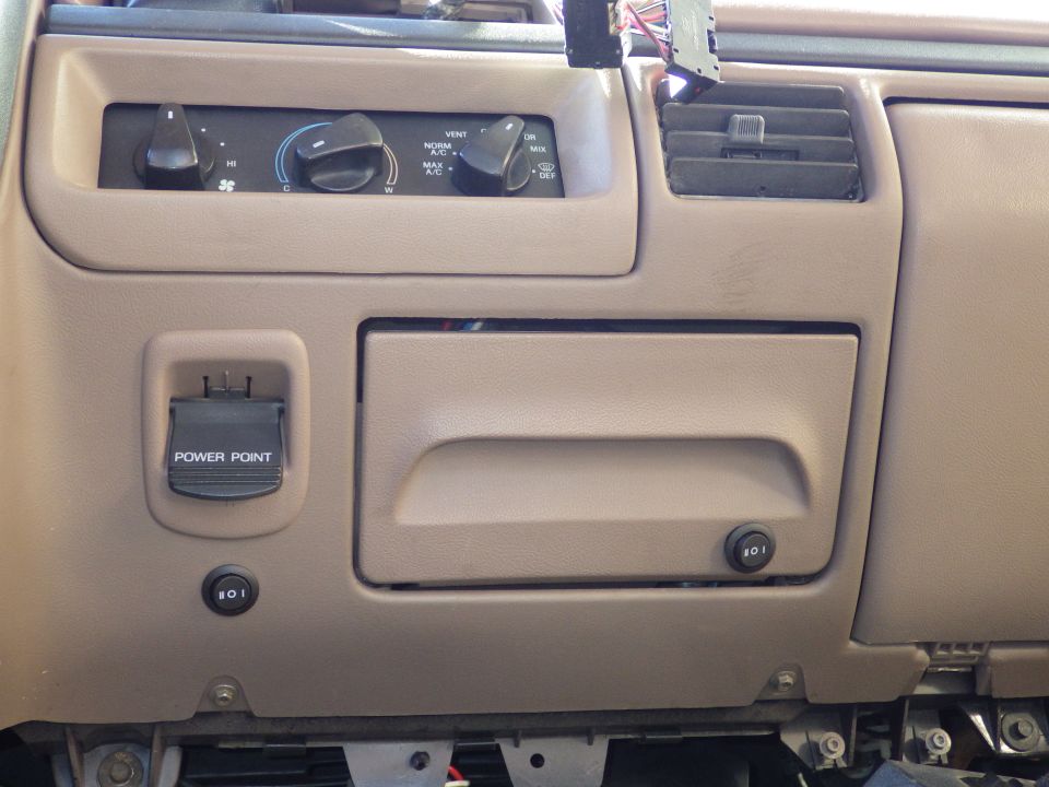 Tan dashboard with HVAC knobs, power point cover, rocker switches and storage pocket
