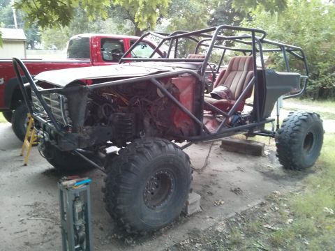 1986 Ford Bronco - This heavily modified vehicle features a custom roll cage and oversized tires, with a red pickup truck visible in the background.