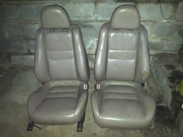 Pair of tan leather car seats with headrests and visible wear
