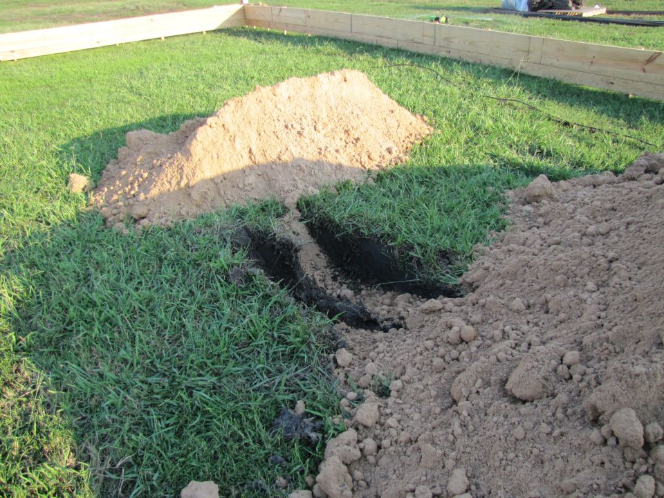 Construction site with dirt piles, trenches, and wooden forms on grass