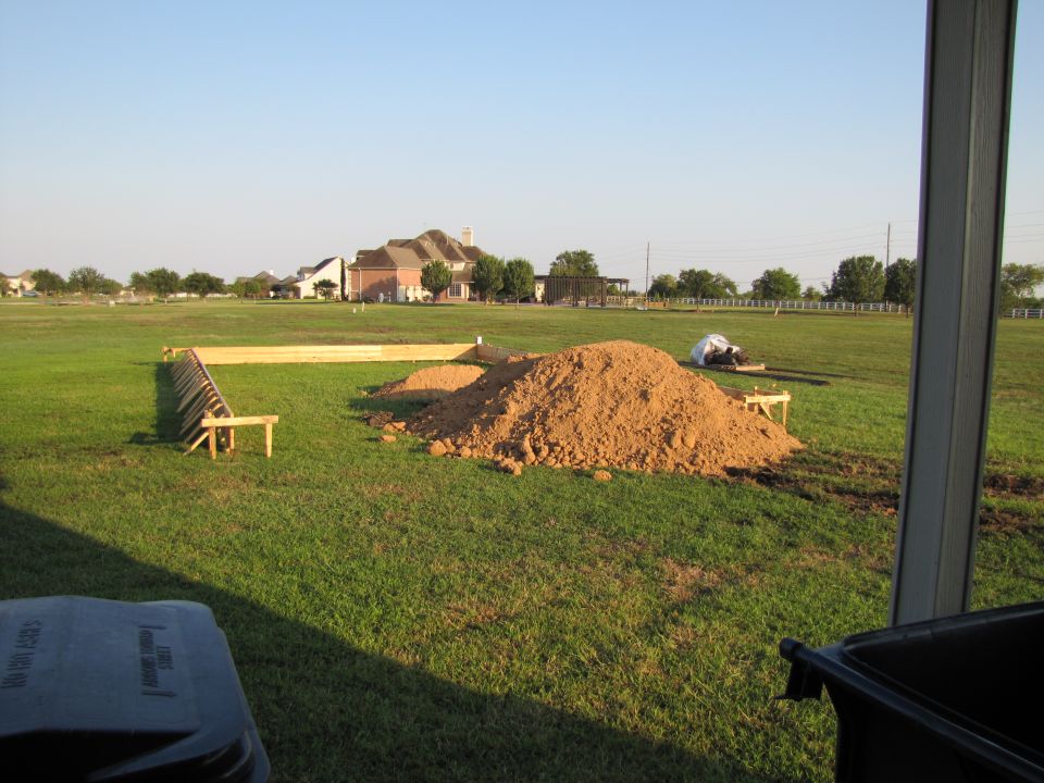 Construction site with wooden frame, dirt pile, and houses in background