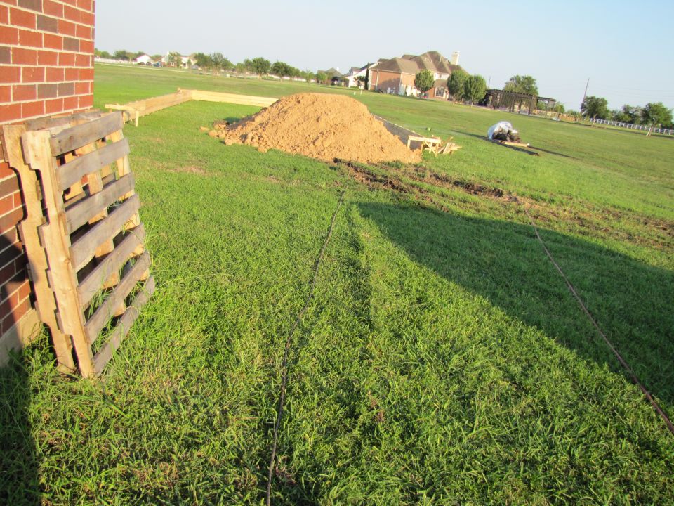 Construction scene with pallets, sand pile, and houses in background. Supermotors.net logo visible