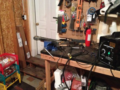 2005 Jeep Wrangler - A single control arm is secured in a vise on a workbench, surrounded by tools and a welding machine.