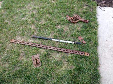 2005 Jeep Wrangler - Several rusty Hi-Lift Jack components are scattered on a grassy area next to a concrete path.