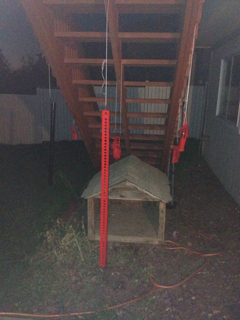 2005 Jeep Wrangler - A red Hi-Lift jack is positioned next to a dog house, with wooden stairs overhead. The scene appears to be outdoors at dusk.