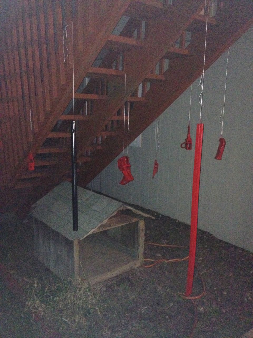 Red painted parts hanging from strings under wooden stairs next to a dog house