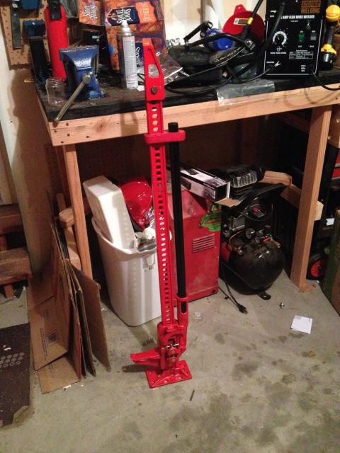 2005 Jeep Wrangler - A red Hi-Lift jack is the central focus, positioned in a workshop environment with tools and equipment in the background.