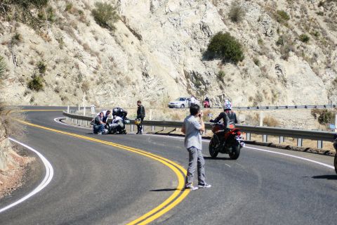1995 Ford Taurus - Several people are gathered around a motorcycle on the side of a winding road, with a car parked further up.