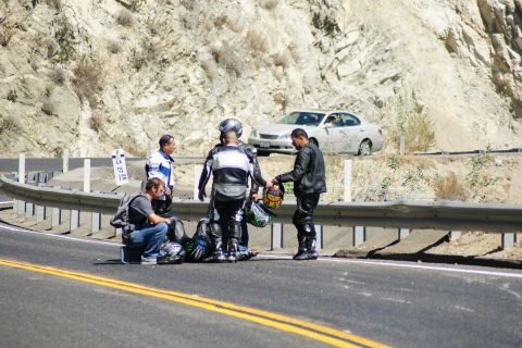 1995 Ford Taurus - Motorcyclists congregate on the side of a road next to a silver sedan parked on an embankment.