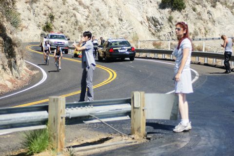 1995 Ford Taurus - A police car is stopped on a winding road, with cyclists and several people observing the scene.