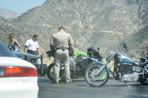 1995 Ford Taurus - A police officer interacts with two men and two motorcycles on the side of a road with mountains in the background.