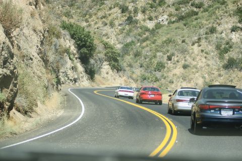 1995 Ford Taurus - A line of cars travels along a winding road bordered by a rocky hillside.