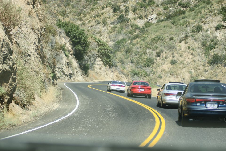 Several cars driving on a two-lane road that curves through a hilly, dry landscape