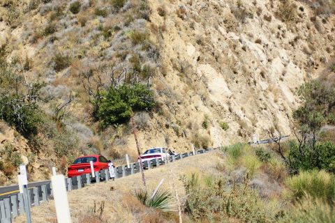 1995 Ford Taurus - Two sedans travel along a scenic, winding road bordered by a steep, dry hillside.