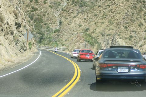 1995 Ford Taurus - Traffic moves along a scenic mountain highway with steep, dry hillsides.