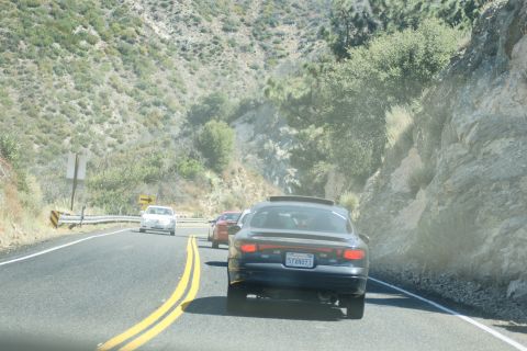 1995 Ford Taurus - A dark sedan with a sunroof drives on a two-lane road through a mountainous landscape, with other vehicles ahead.
