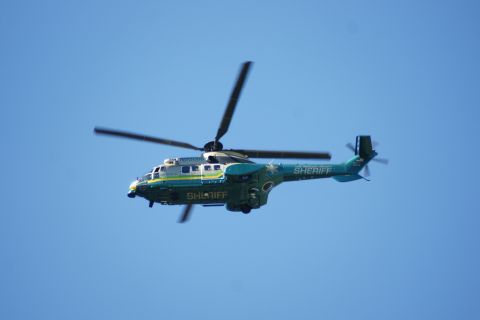 1995 Ford Taurus - A sheriff helicopter with "SHERIFF" written on its side flies through a clear blue sky.