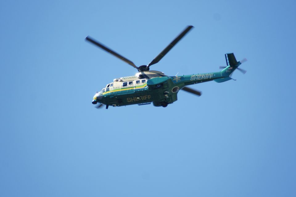 Sheriff helicopter flying in a clear blue sky. It is green and white with 'SHERIFF' written on the side