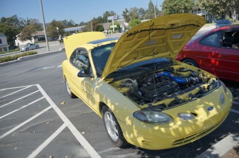 1995 Ford Taurus - Yellow Ford Escort with hood open, parked next to a red car.