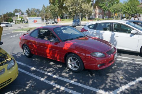 1995 Ford Taurus - A red coupe is parked in a lot with other vehicles visible.
