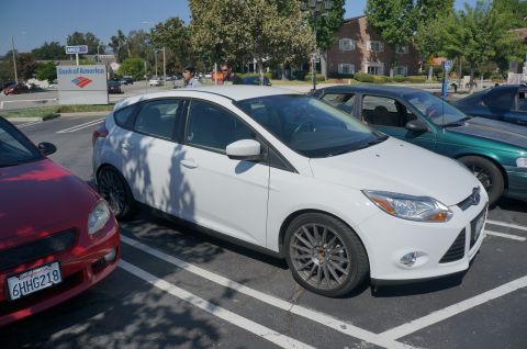 1995 Ford Taurus - A white Ford Focus hatchback is parked in a lot next to other vehicles.