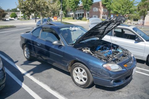 1995 Ford Taurus - Blue coupe with hood open, showing engine modifications. A silver sedan is parked nearby.